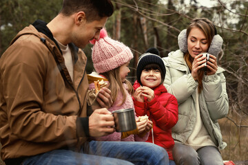 Happy family with sandwiches and hot drinks spending time together in forest