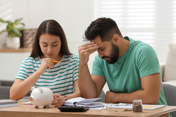 Worried young couple planning family budget at wooden table indoors