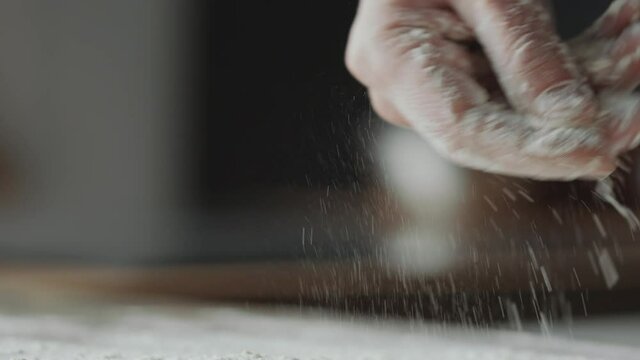 Close up selective focus shot of male hand sprinkling flour on table