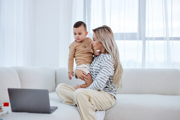 young female take a break after online work on laptop, spend time with child son, sit on sofa together, hugging, enjoying free time together. in bright cozy modern living room, at home, domestic