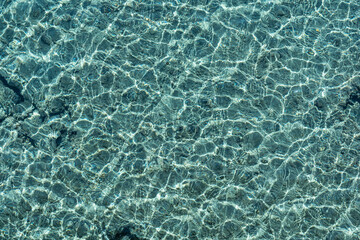 Clear water background. Top view of completely transparent sea water with sun reflections