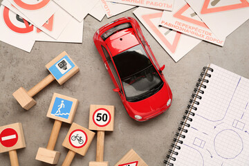 Many different road signs, notebook with sketch of roundabout and toy car on grey table, flat lay. Driving school