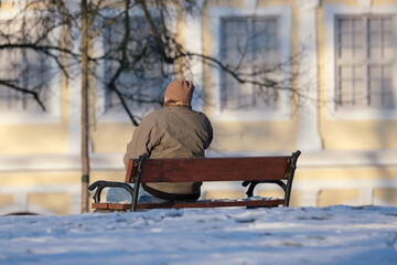 Ältere Person, die auf einer Bank sitzend in einem Park die winterliche Landschaft genießt