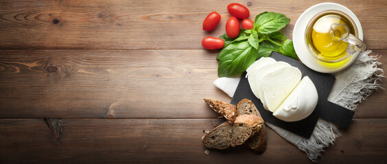 Buffalo mozzarella, bread, cherry tomatoes, extra virgin olive oil and basil on wooden background, top view, space for text.