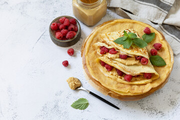 Healthy breakfast, celebrating Pancake day. Delicious homemade crepes with rasberries and peanut paste on a stone tabletop. Copy space.