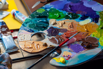 Palette with oil paints and a brush. Painting process, art workshop. Different paint colors applied...