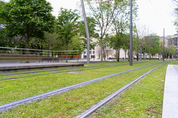 Streetcar rails over green grass by station in Bilbao city. Tram tracks melted into natural environment, nobody on street concepts