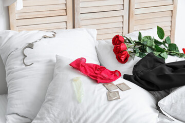 Female panties with condoms, handcuffs, roses and clothes on bed after romantic date