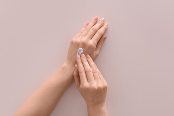 Female hands with cosmetic cream on light background