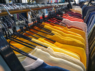 Clothes hanging on hangers in a row, multi-colored sweaters hanging in the store