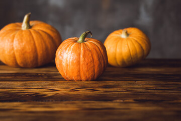 Three orange pumpkins on the brown table and grey background. Selective focus.