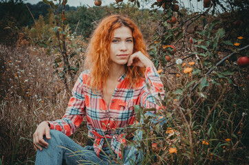 Attractive beautiful slender woman with wavy red hair and blue eyes in an apple orchard. Autumn bright background.