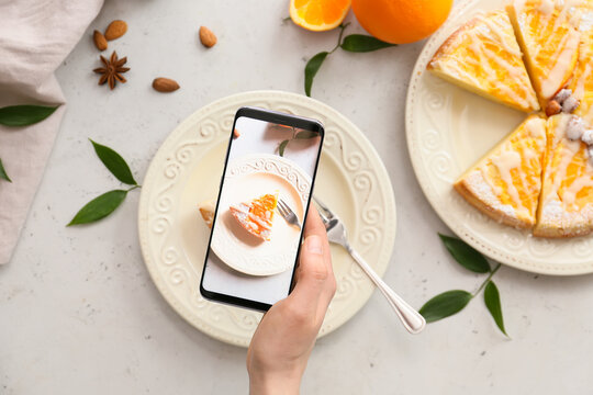 Woman with mobile phone taking photo of tasty citrus cake on table