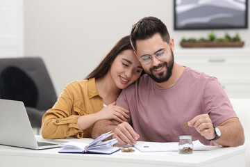 Happy young couple counting money at white table indoors