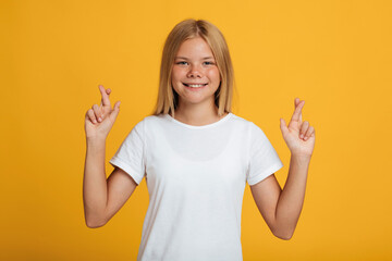 Smiling young caucasian female schoolgirl in white t-shirt crossed her fingers and makes a wish