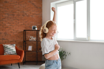 Little redhead girl in headphones dancing at home