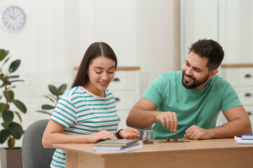 Fototapeta premium Happy young couple counting money at wooden table indoors