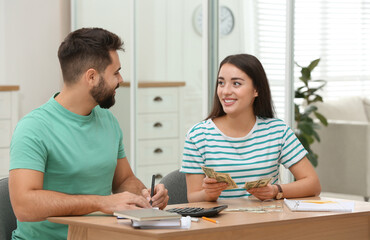 Obraz premium Happy young couple counting money at wooden table indoors