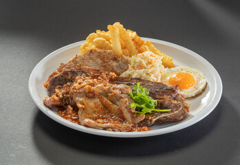 Traditional mixed grill platter Grilled Lamb Chop, chicken cutlet, chicken chop, french fries, eggs and salad in white dish on dark grey background