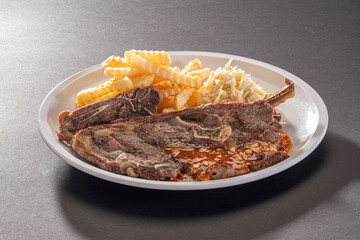 Organic Grilled Lamb Chop sauce with french fries and salad in white dish on dark grey background top view