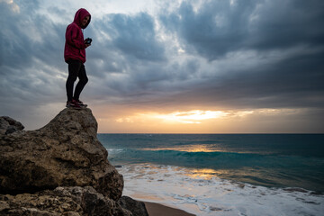 Young man standing on a rock watching waves breaking at the Cape of Trafalgar in a dramatic stormy...
