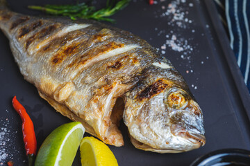 Grilled dorado fish on a plate with vegetables, lemon and a glass of white wine.