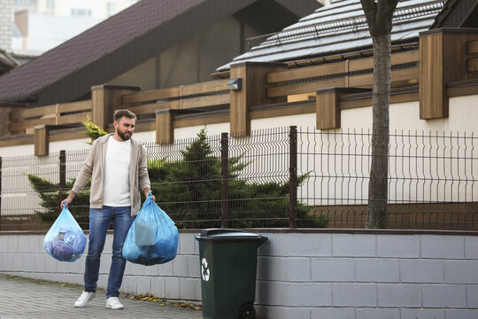 Man carrying garbage bags to recycling bin outdoors