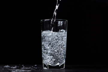 Mineral water is poured into a glass on a black background. Useful drinking mineral water.