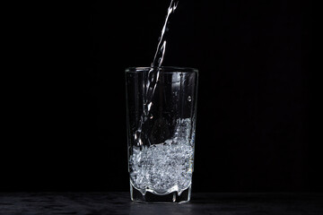 Mineral water is poured into a glass on a black background. Useful drinking mineral water.