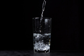 Mineral water is poured into a glass on a black background. Useful drinking mineral water.