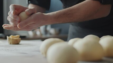 Close up selective focus shot of male baker forming dough balls while preparing bread buns