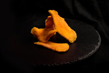 Dried slices of mango fruit on black background.	
