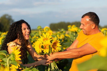 A beautiful young couple a man and a woman, embrace in a field of sunflowers at sunset.