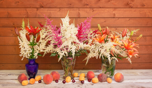 Beautiful bouquets of astilbe and lily flowers in vases  and fresh fruits.