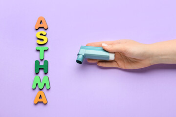 Word ASTHMA and female hand with inhaler on color background