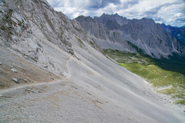 Mountain path between cliffs and screes leads into the distance.