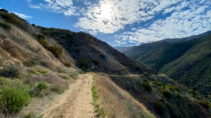 Hiking trail leading down to a winding section through Santa Monica Mountains at Point Mugu State Park, California. Lots of small clouds in sky