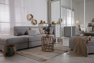 Comfortable grey sofa, ottoman and wardrobe with mirror doors in living room interior