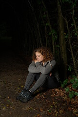 Frau sitzt im dunklen Wald, nachdenklich und deprimiert