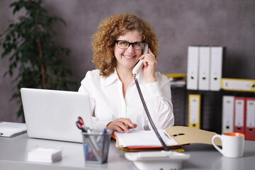 Sekretärin mit Brille sitzt am Schreibtisch und telefoniert