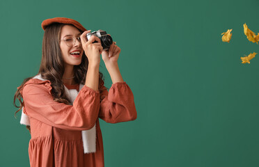 Beautiful Parisian woman taking pictures of autumn leaves on green background