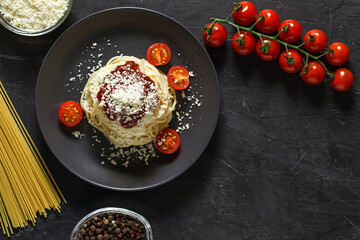 Pasta spaghetti Italian with parmesan and ingredients for cooking, tomatoes, spices, macaroni, grated cheese, top view dark background, with space to copy text.