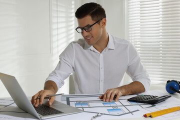 Architect working with construction drawings and laptop in office