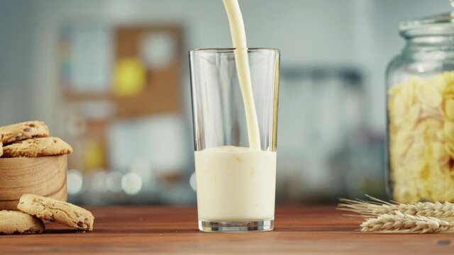 Yogurt are pouring into a glass cup from bottle. Glass with Kefir, milk or Turkish Ayran stands on a wooden table.
