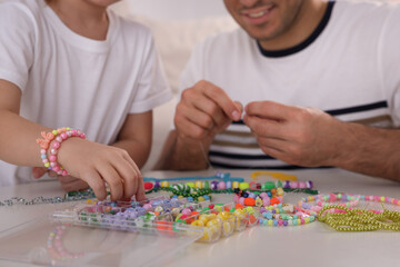 Father with his daughter making beaded jewelry at table, closeup - obrazy, fototapety, plakaty