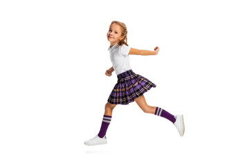 Portrait of cute little girl, pupil in school uniform running isolated on white background. Concept of childhood, emotions, study