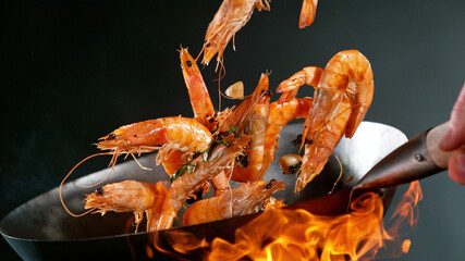 Closeup of chef throwing prawns from wok pan in fire.
