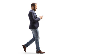 Full length profile shot of a young man in suit and jeans walking and typing on a mobile phone