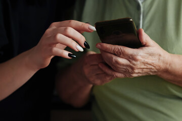 A young girl helps an elderly woman deal with a modern telephone and the Internet, make purchases online, use a social network and be always in touch