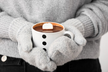 Woman holding cup of tasty hot chocolate with marshmallow on light background